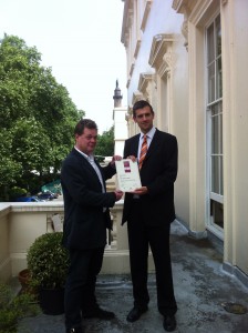 Alastair Swanwick standing on the balcony of the The Institute of Minerals, Materials & Mining, London presenting the Plastic Design Award to James Scott.